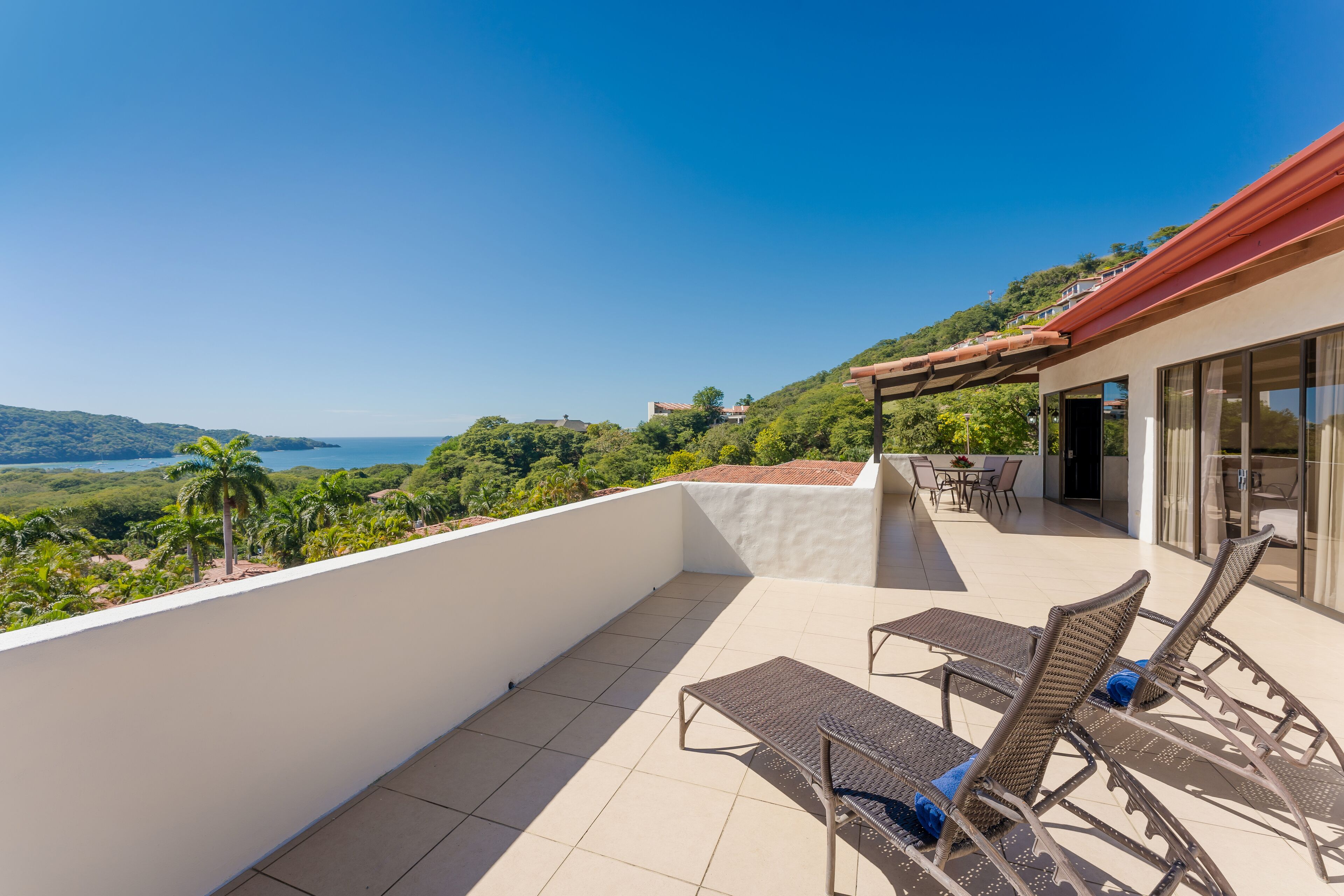 A balcony with two wicker lounge chairs, a table, and a view of a green landscape and water.