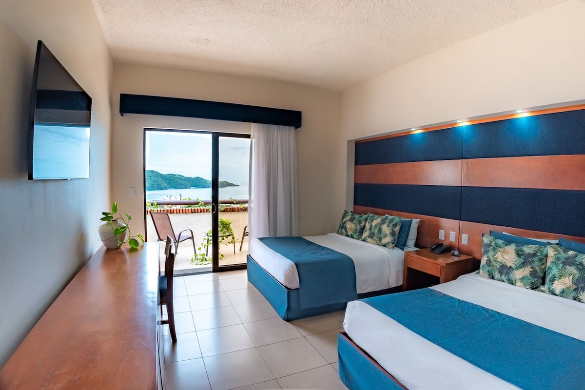 A hotel room with two beds, a dining table, a TV, and a view of the outdoors.