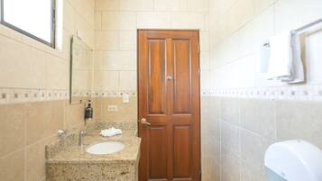 Une salle de bain avec un lavabo doté d’un plan de travail en granit, une porte en bois, un miroir et un sèche-mains.