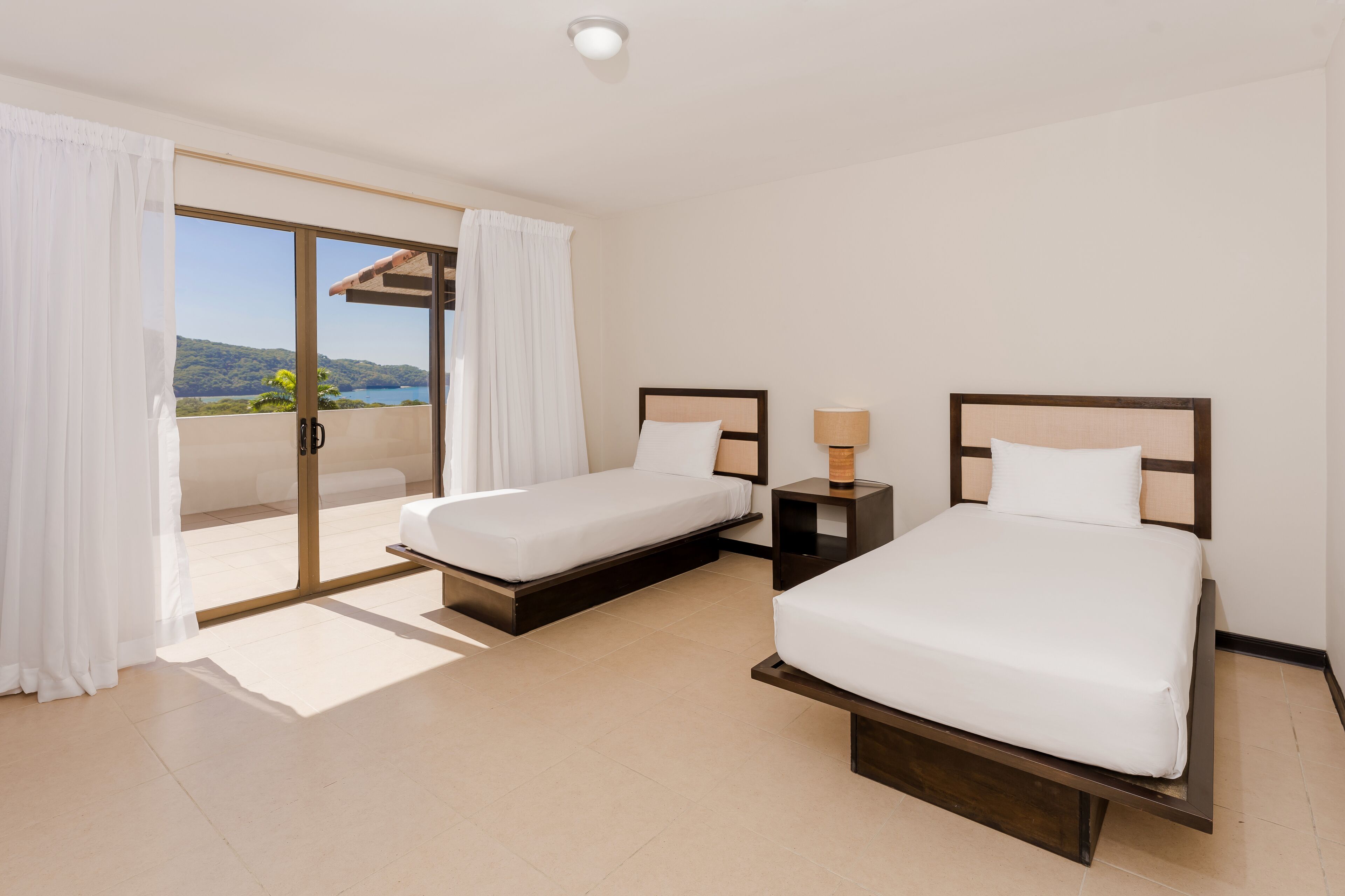 A hotel room with two beds, a sliding glass door to a balcony, and a ceiling light.