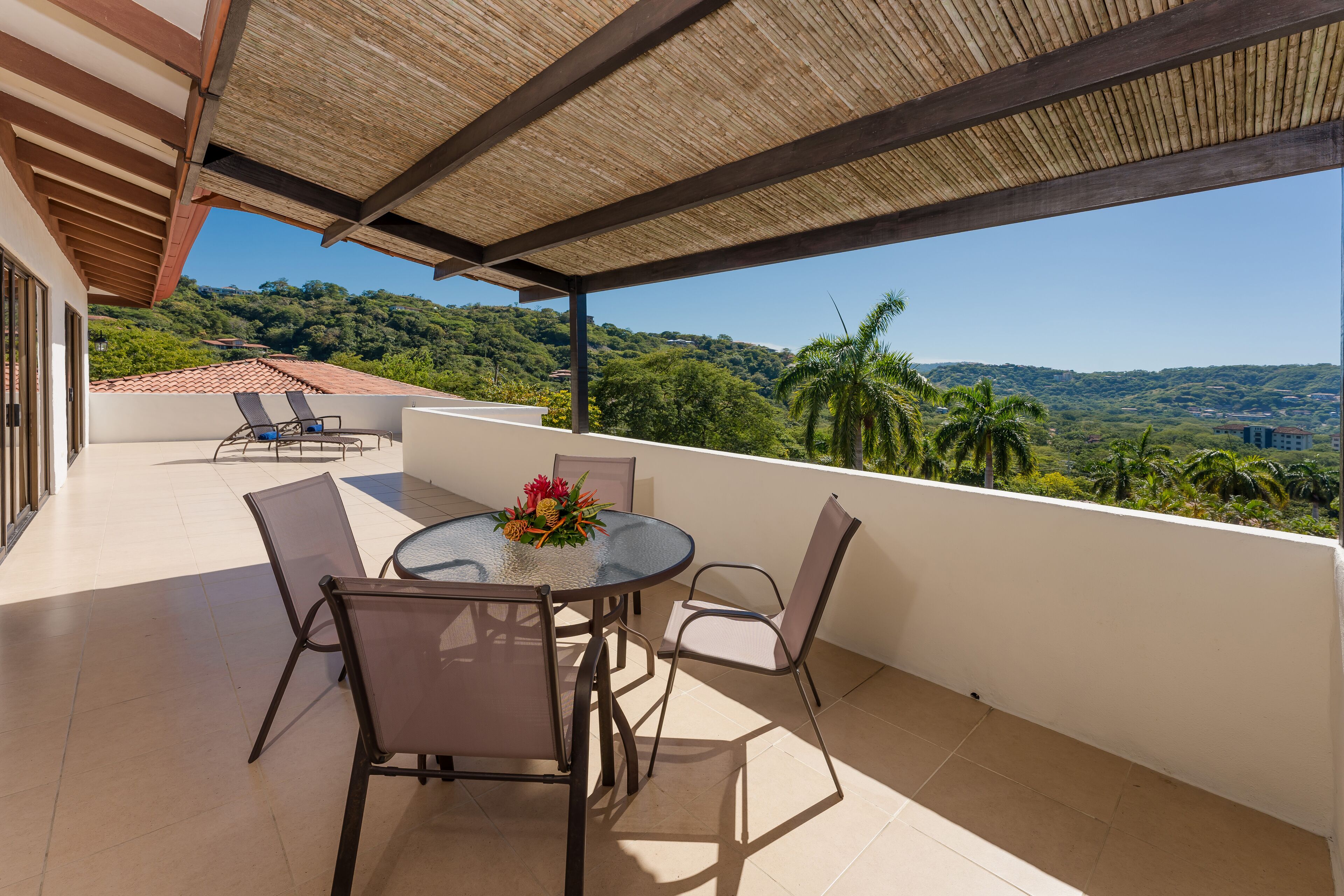 Ein überdachter Außenbereich mit Tisch und Stühlen, mit Blick auf eine üppige Landschaft.