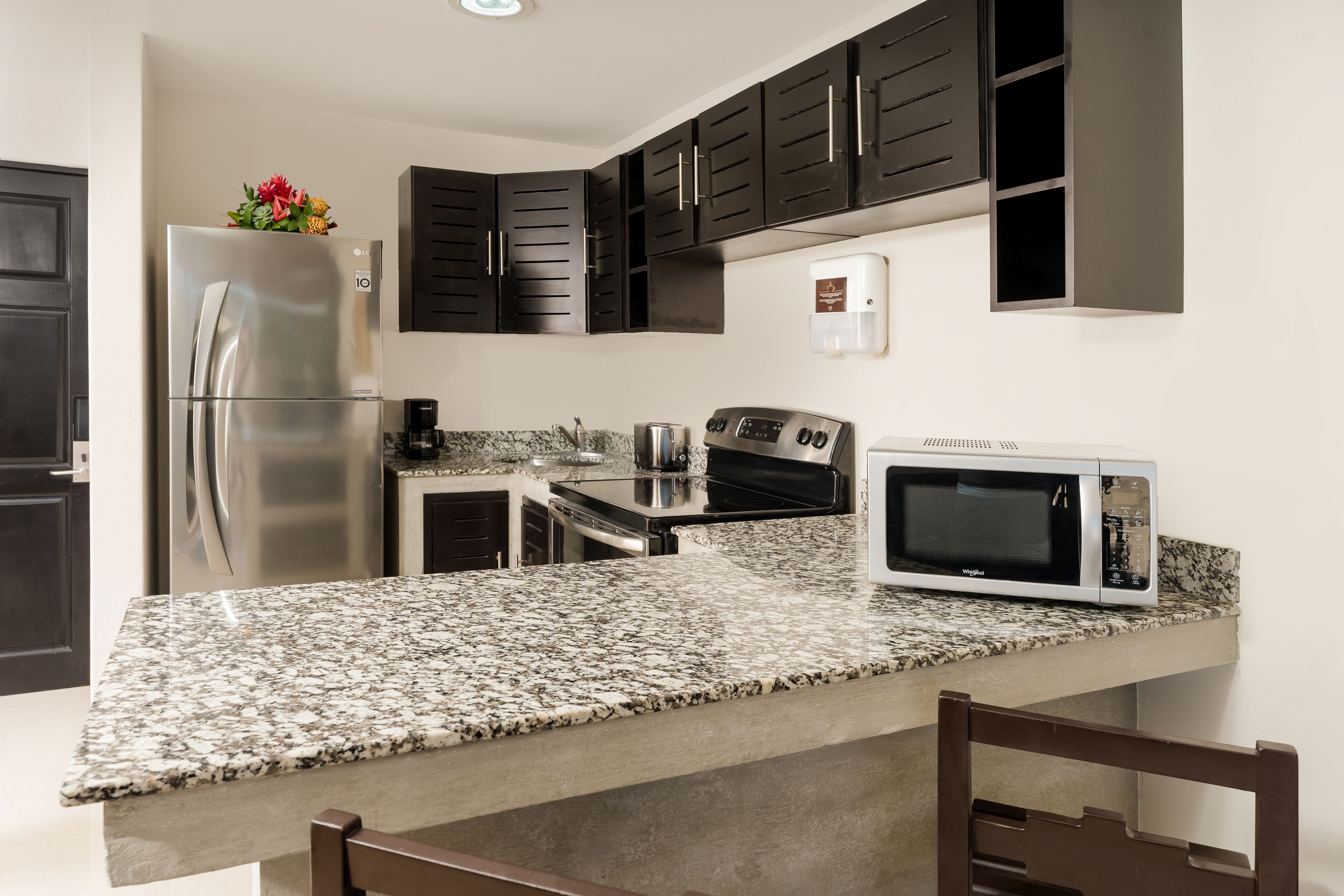 Uma cozinha moderna com armários escuros, uma geladeira de aço inoxidável, micro-ondas e bancadas de granito.