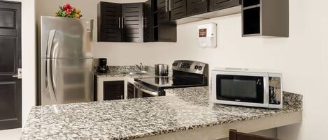 A modern kitchen with dark cabinets, a stainless steel refrigerator, a microwave, and granite countertops.