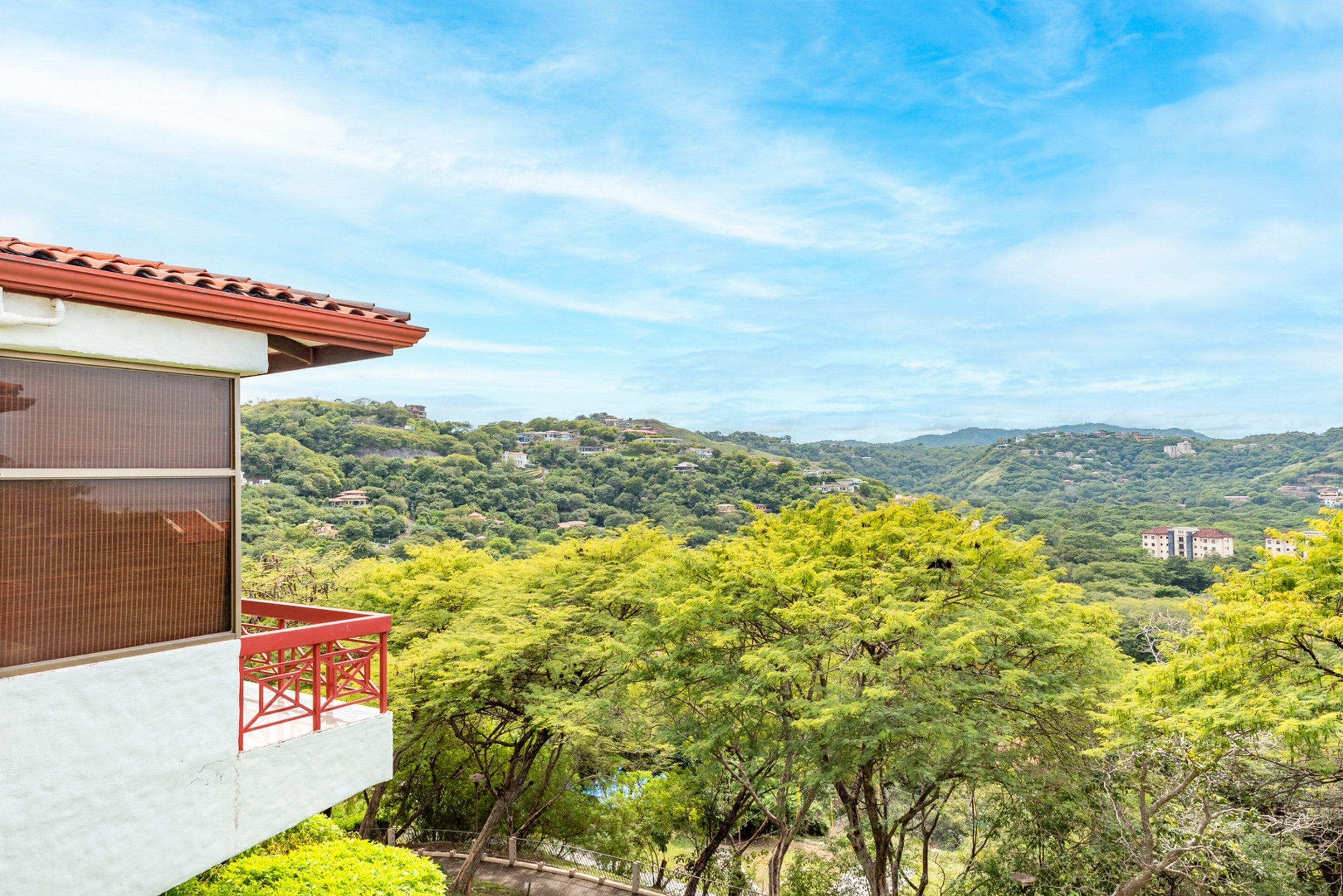 A modern building with a red balcony overlooking a lush green landscape with hills in the distance.