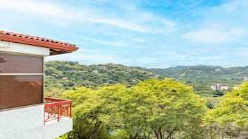 A modern building with a red balcony overlooking a lush green landscape with hills in the distance.