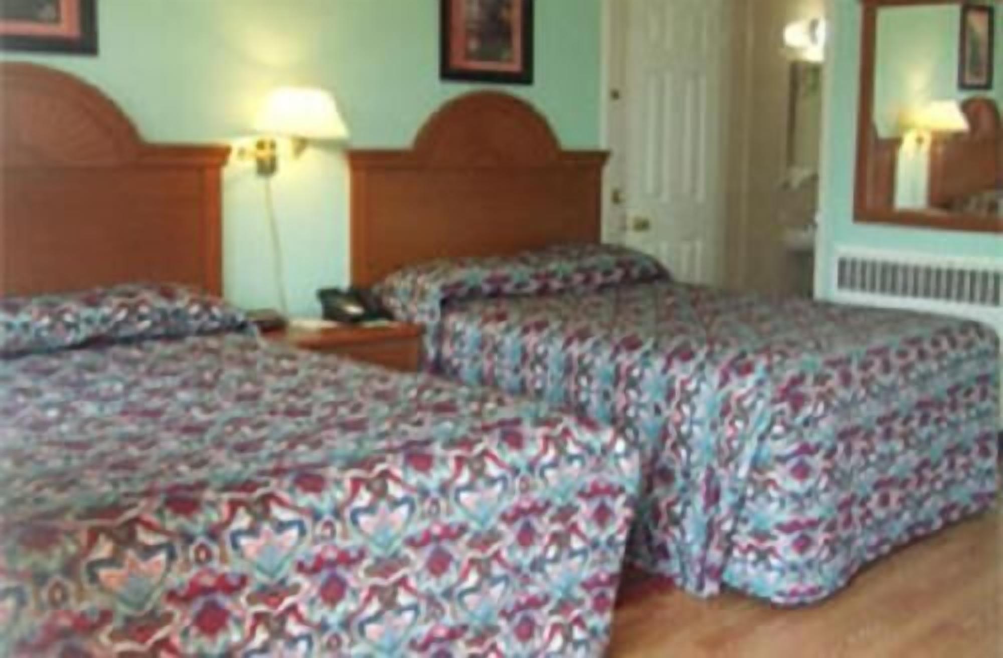 Habitación de hotel con dos camas, cada una con ropa de cama estampada. Se observan mesitas de noche con lámparas, una puerta y un radiador.