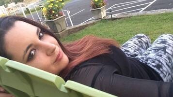Una persona recostada en una silla verde al aire libre, con una carretera y macetas de flores al fondo.