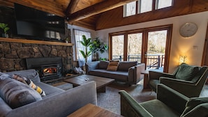 A cozy living room with a stone fireplace, comfortable seating, and a large window offering a view of the outdoors. - The Boha Hotel (Lake Placid)