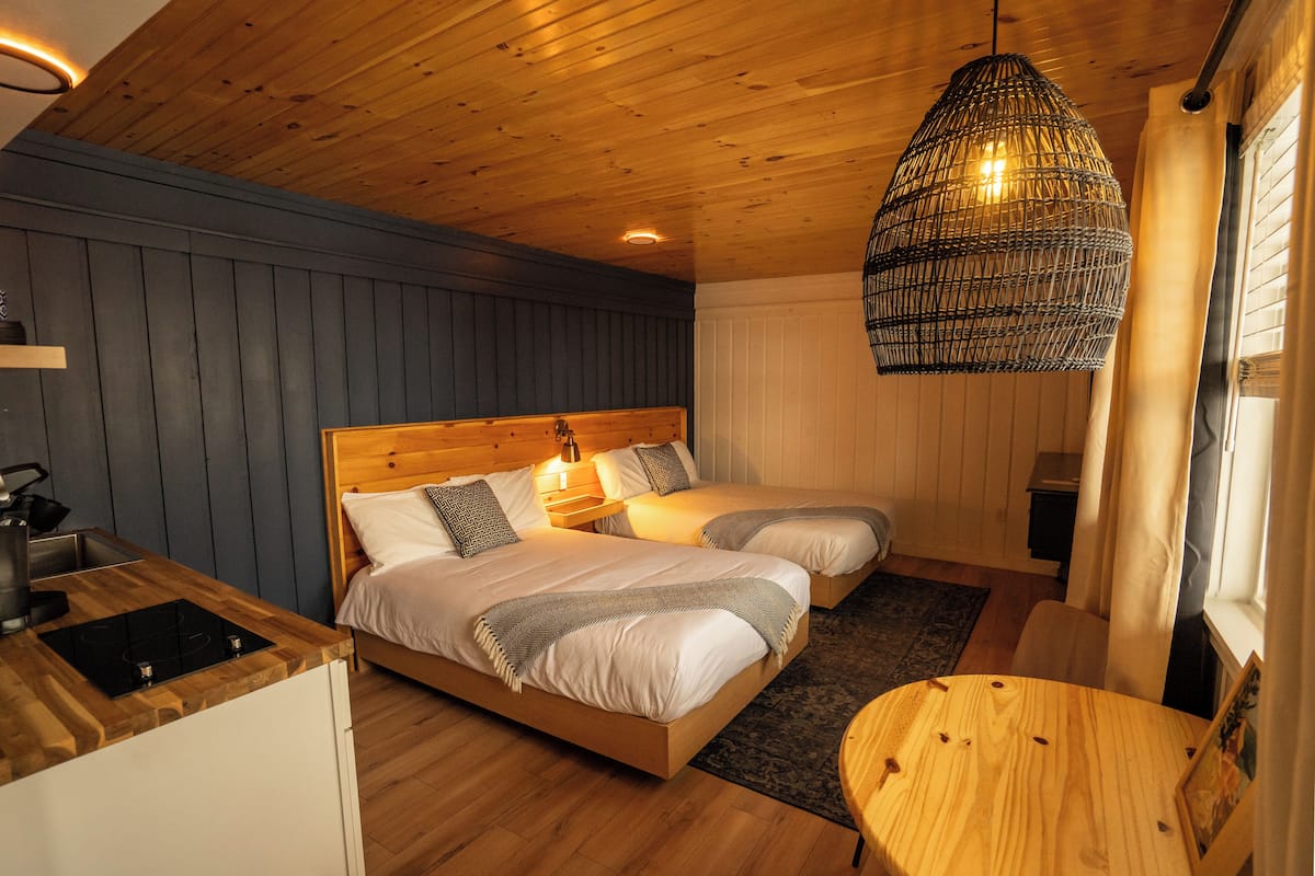 A cozy room with two beds, a wooden ceiling, a hanging light fixture, and a small table.