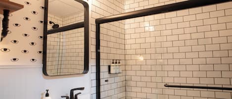A bathroom with a white sink, black faucet, and a mirror with a black frame. There are white tiles on the walls and a black towel rack.