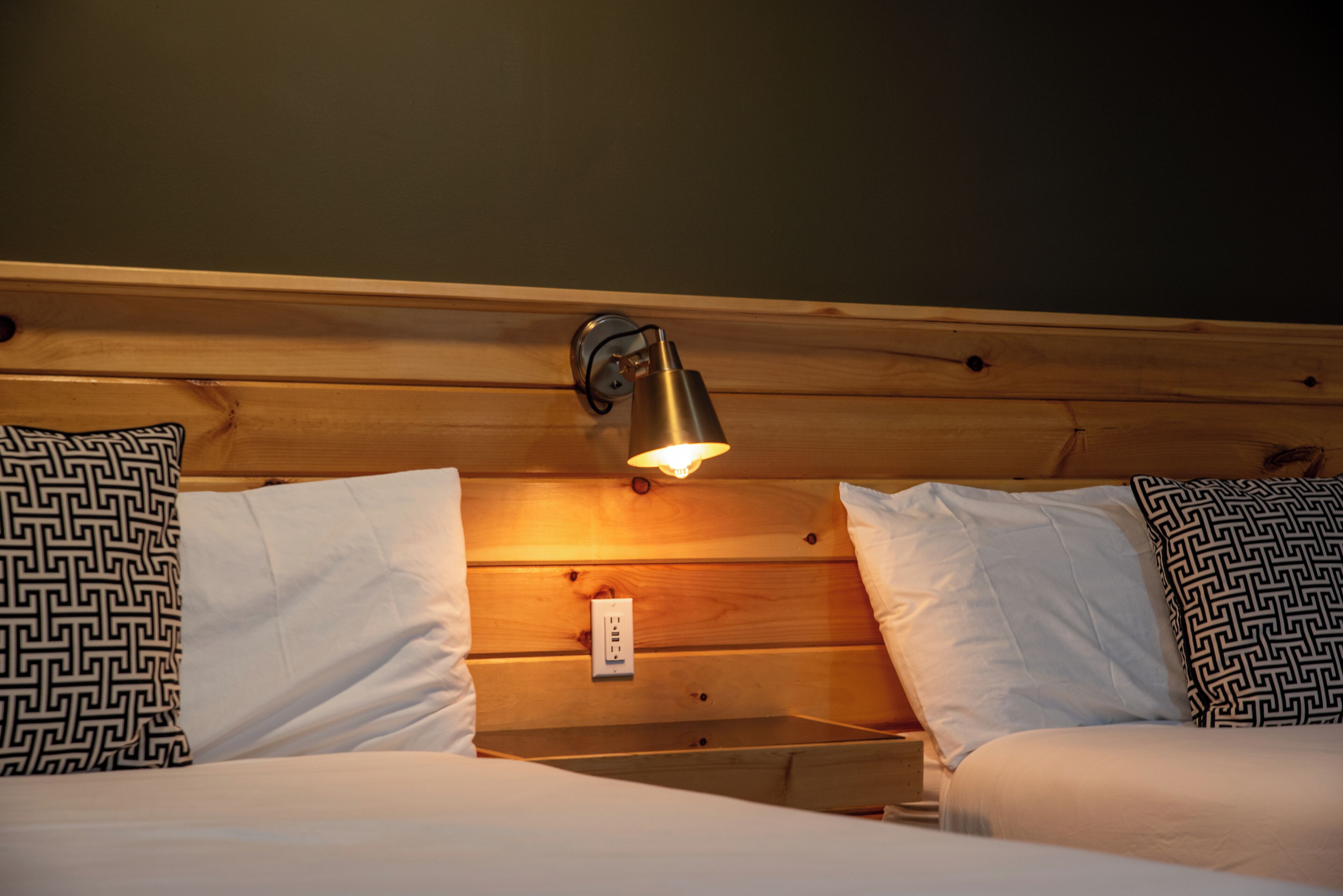 A wooden headboard with a wall-mounted light fixture and a power outlet.