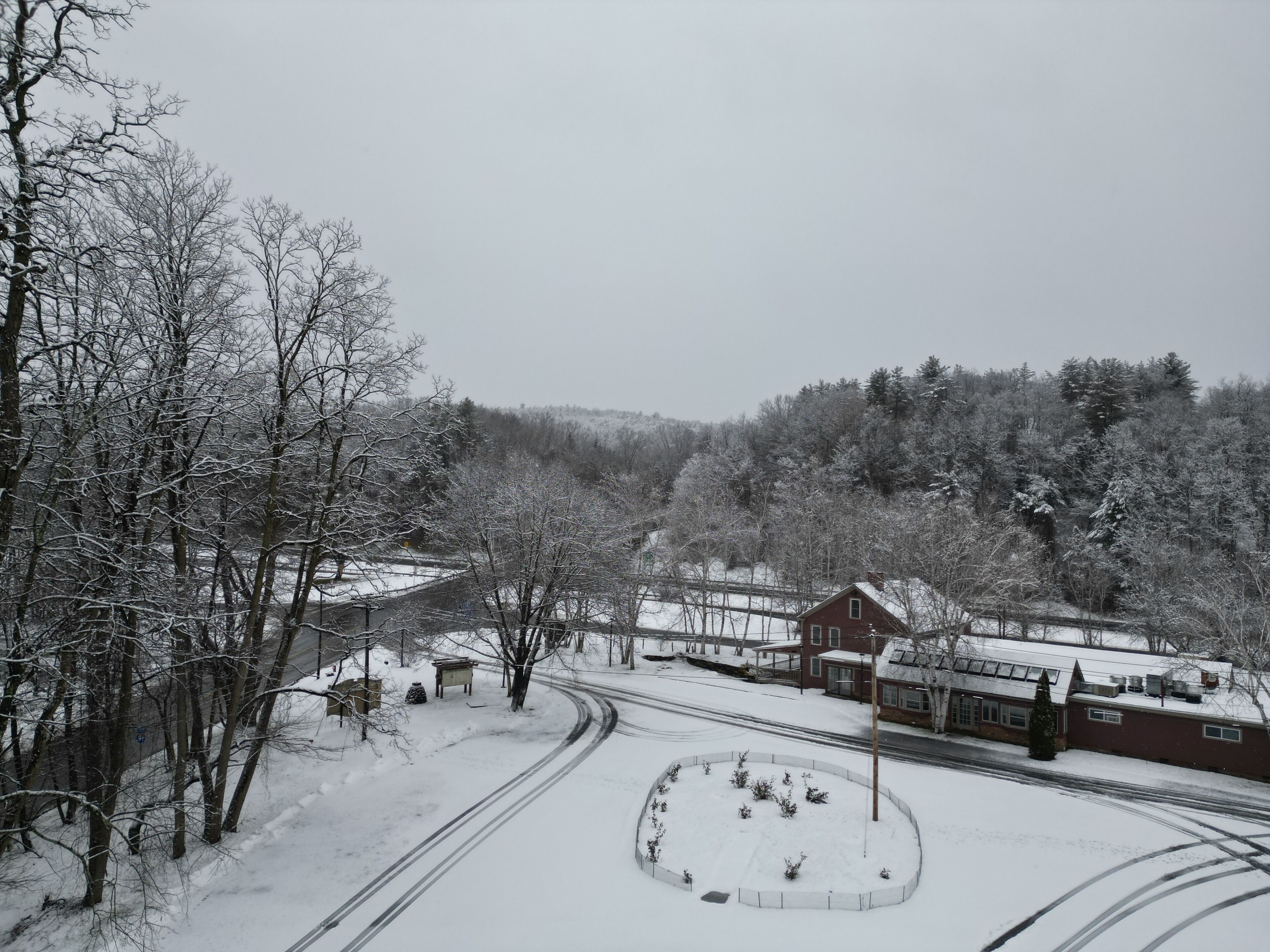 A snow-covered landscape with a road, a circular park area, and a red building with a gabled roof.