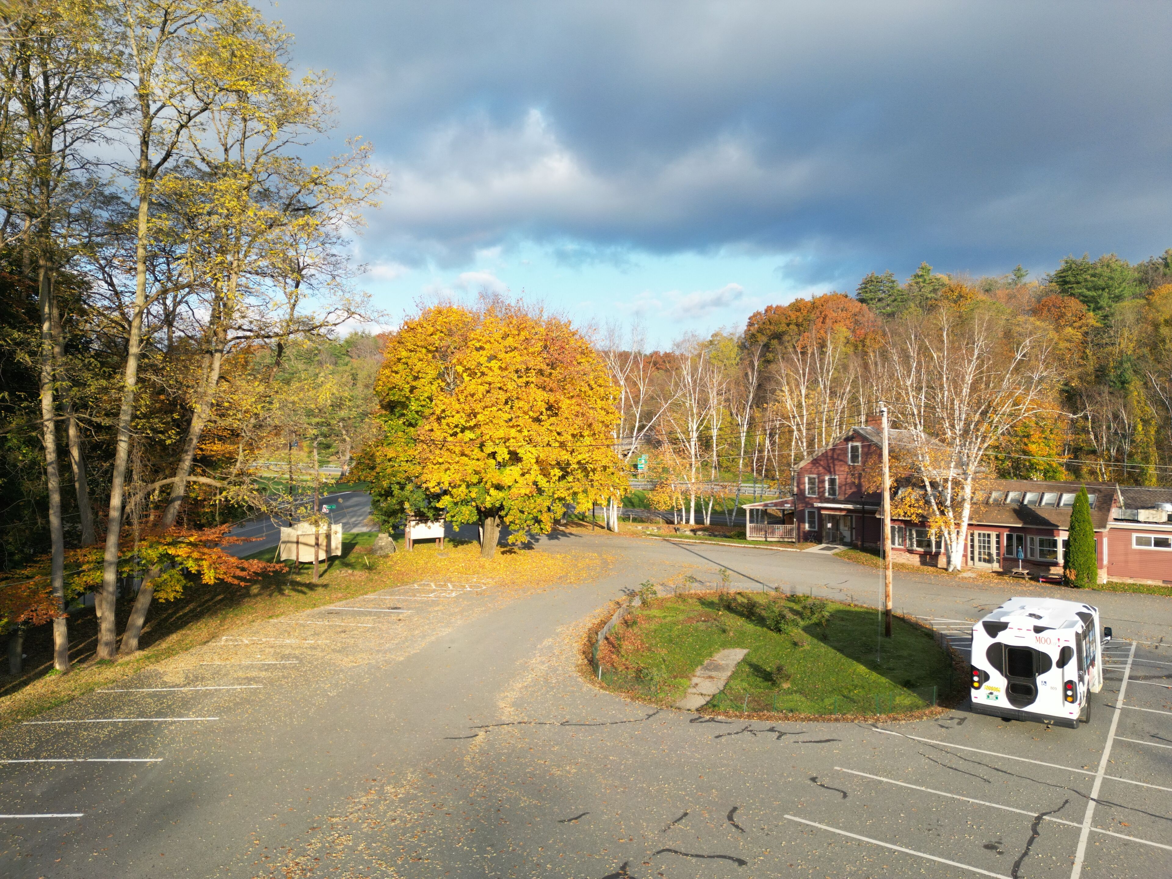 Un parking avec un autobus, un bâtiment doté d’un porche et des arbres aux feuilles d’automne.