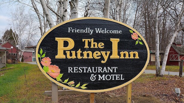 Señal del Putney Inn, un restaurante y motel, con un mensaje de bienvenida amigable y decoraciones florales.