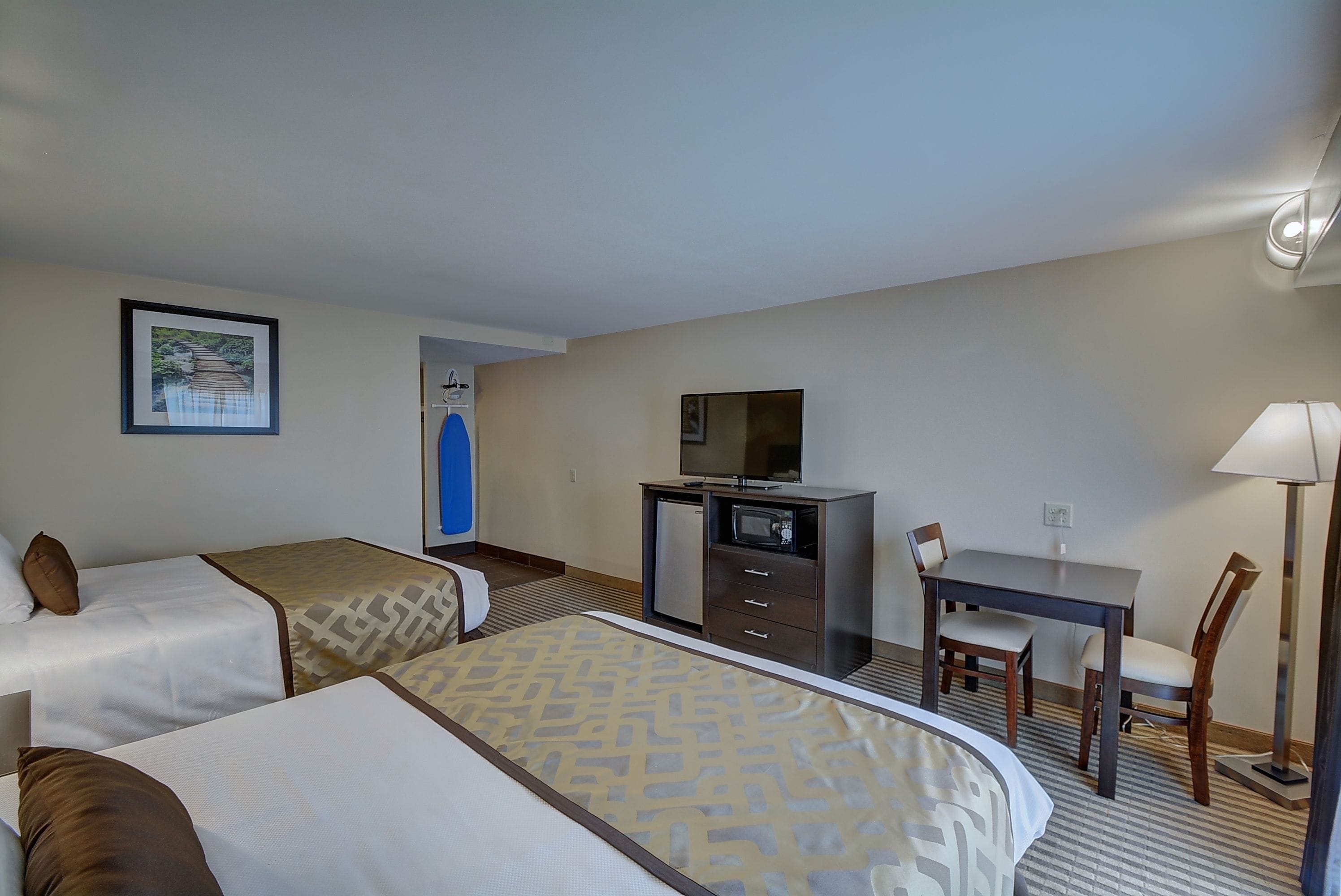 Una habitación de hotel con dos camas, un escritorio con silla, un televisor y una lámpara.