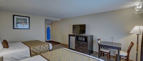 A hotel room with two beds, a desk with a chair, a television, and a lamp.