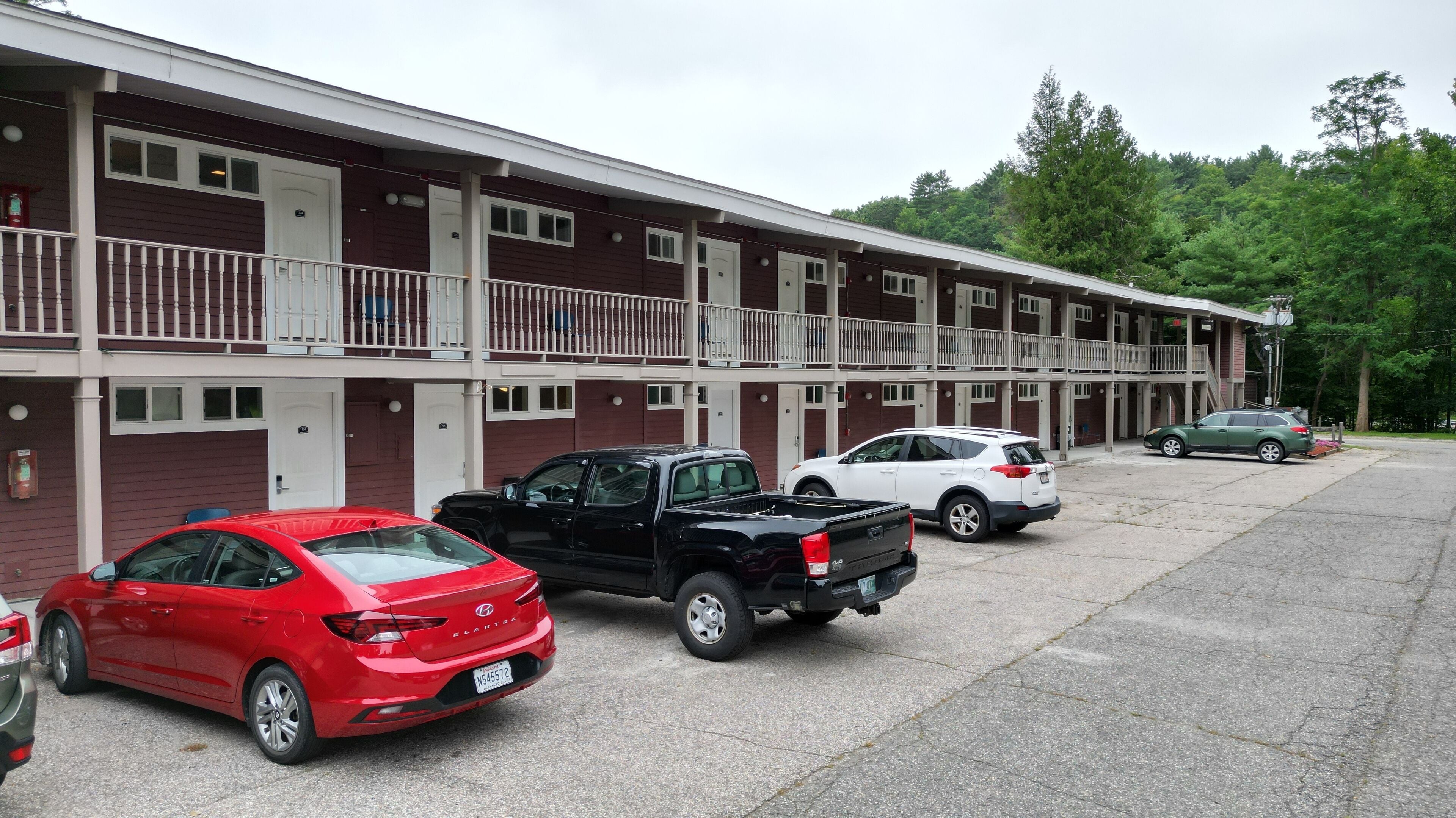 Ein Motel mit einer Reihe von Zimmern, jedes mit einem Balkon. Vor dem Haus sind mehrere Autos geparkt.