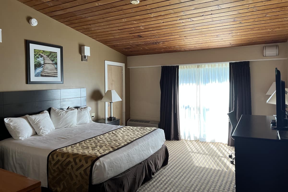 Une chambre d’hôtel avec un plafond en bois, un lit recouvert d’une courtepointe à motifs, un bureau avec un ordinateur et une fenêtre avec des rideaux.