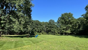 Un campo cubierto de hierba con un parque infantil y árboles al fondo.