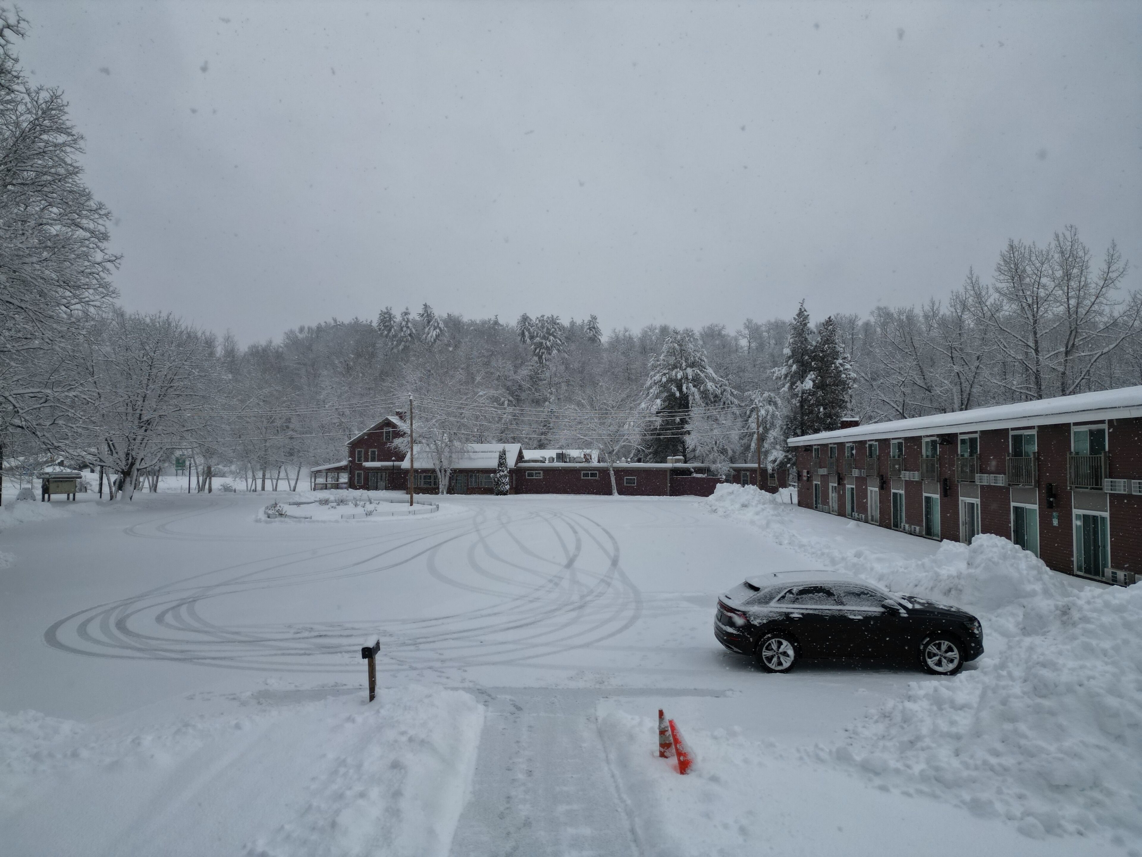 A snow-covered parking lot with a building and trees in the background.