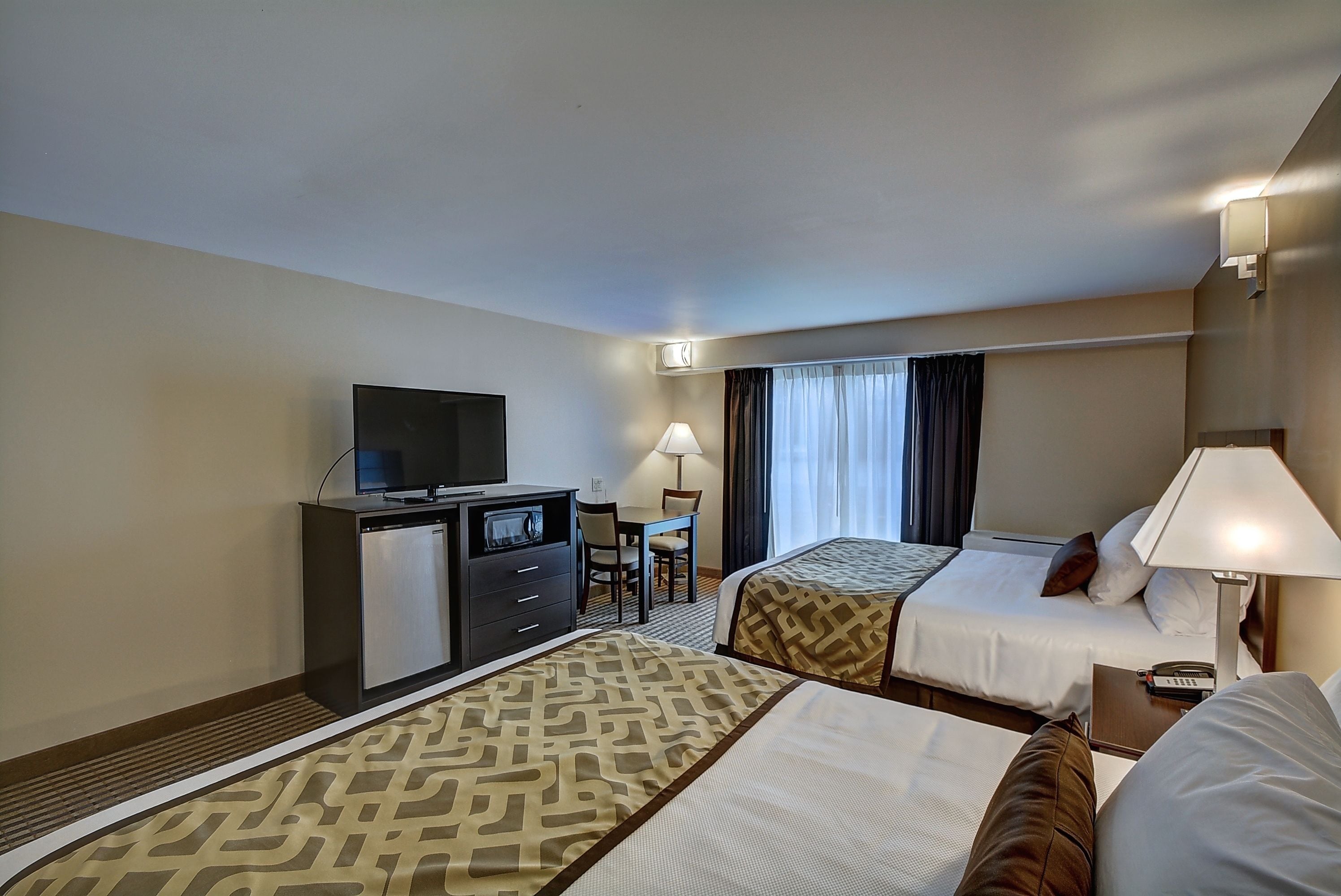 A hotel room with two beds, a desk, a television, and a lamp.