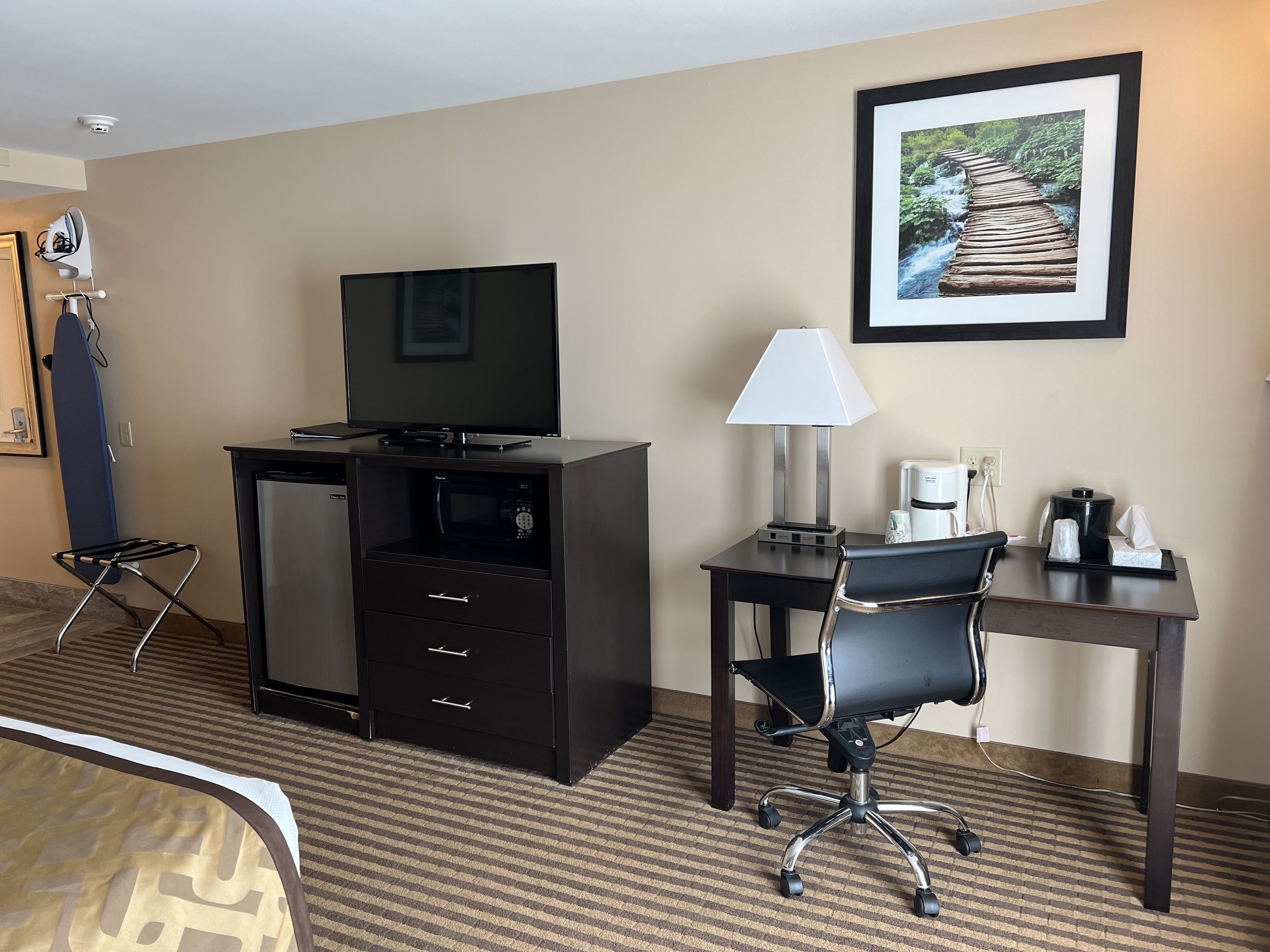 Habitación de hotel con escritorio, silla, televisor, microondas y un cuadro en la pared.