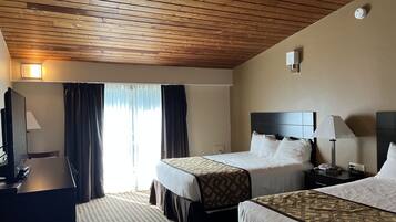 A hotel room with two beds, a desk, a TV, and a window with curtains.