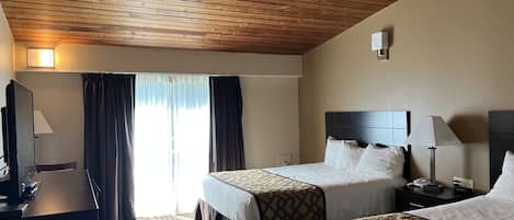 A hotel room with two beds, a desk, a TV, and a window with curtains.