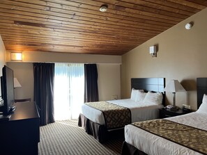 A hotel room with two beds, a desk, a TV, and a window with curtains.