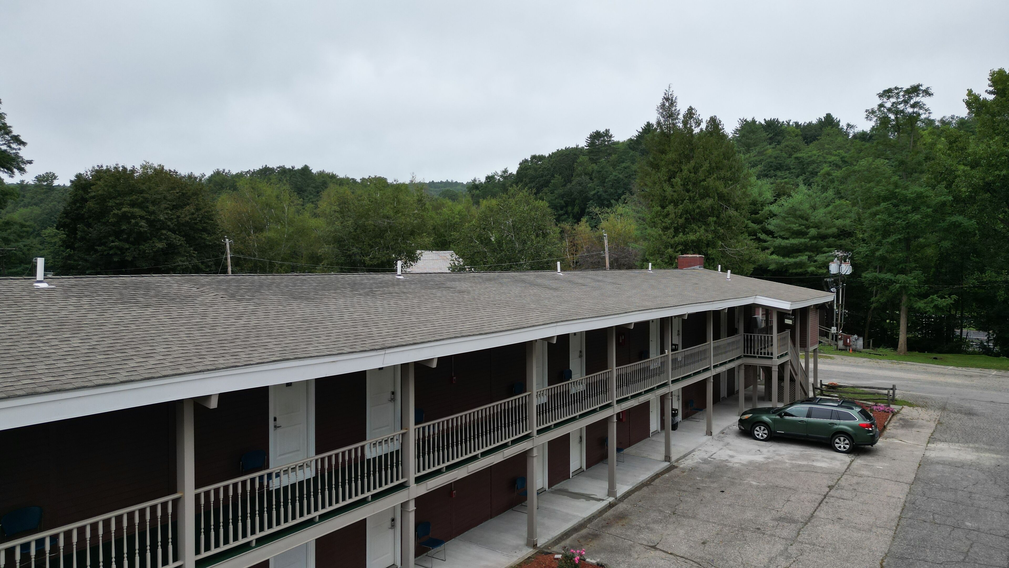A two-story motel with a flat roof, a covered front porch, and a parking area with a green car.