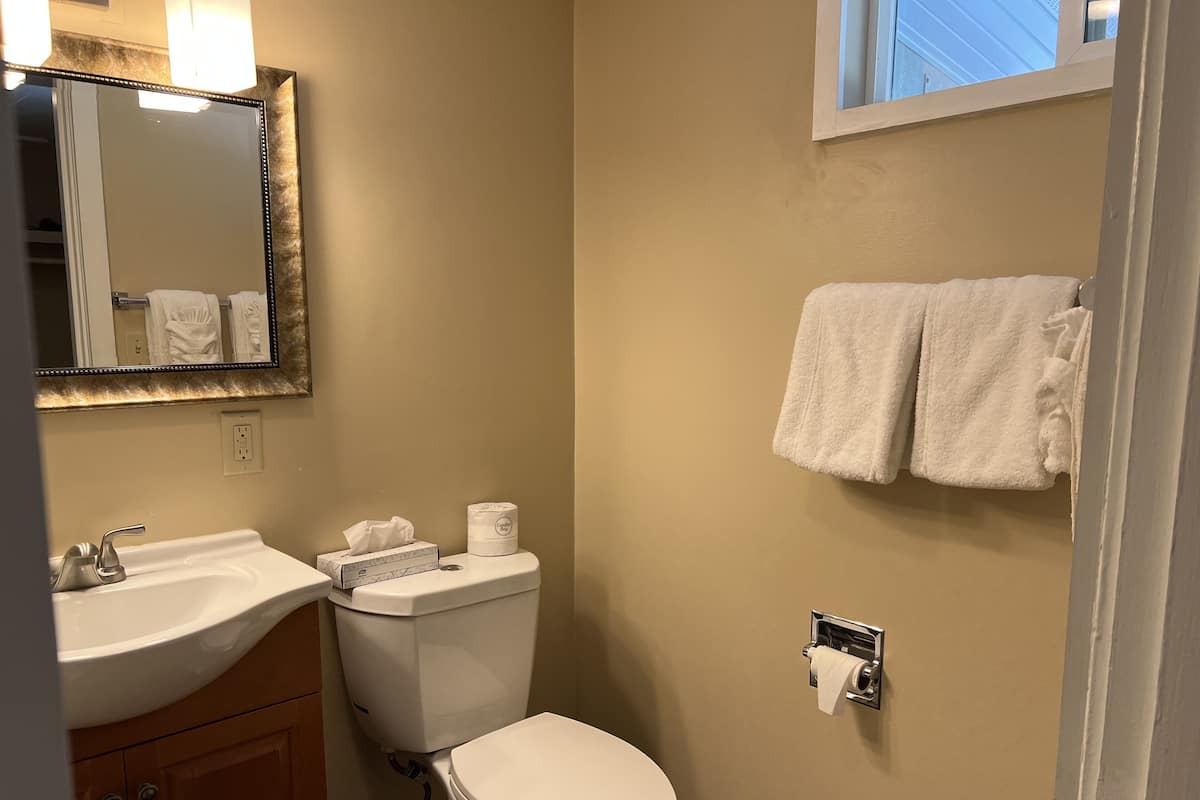 Une salle de bain avec un lavabo, des toilettes et un miroir. Des serviettes sont accrochées au mur et il y a une fenêtre au-dessus des toilettes.