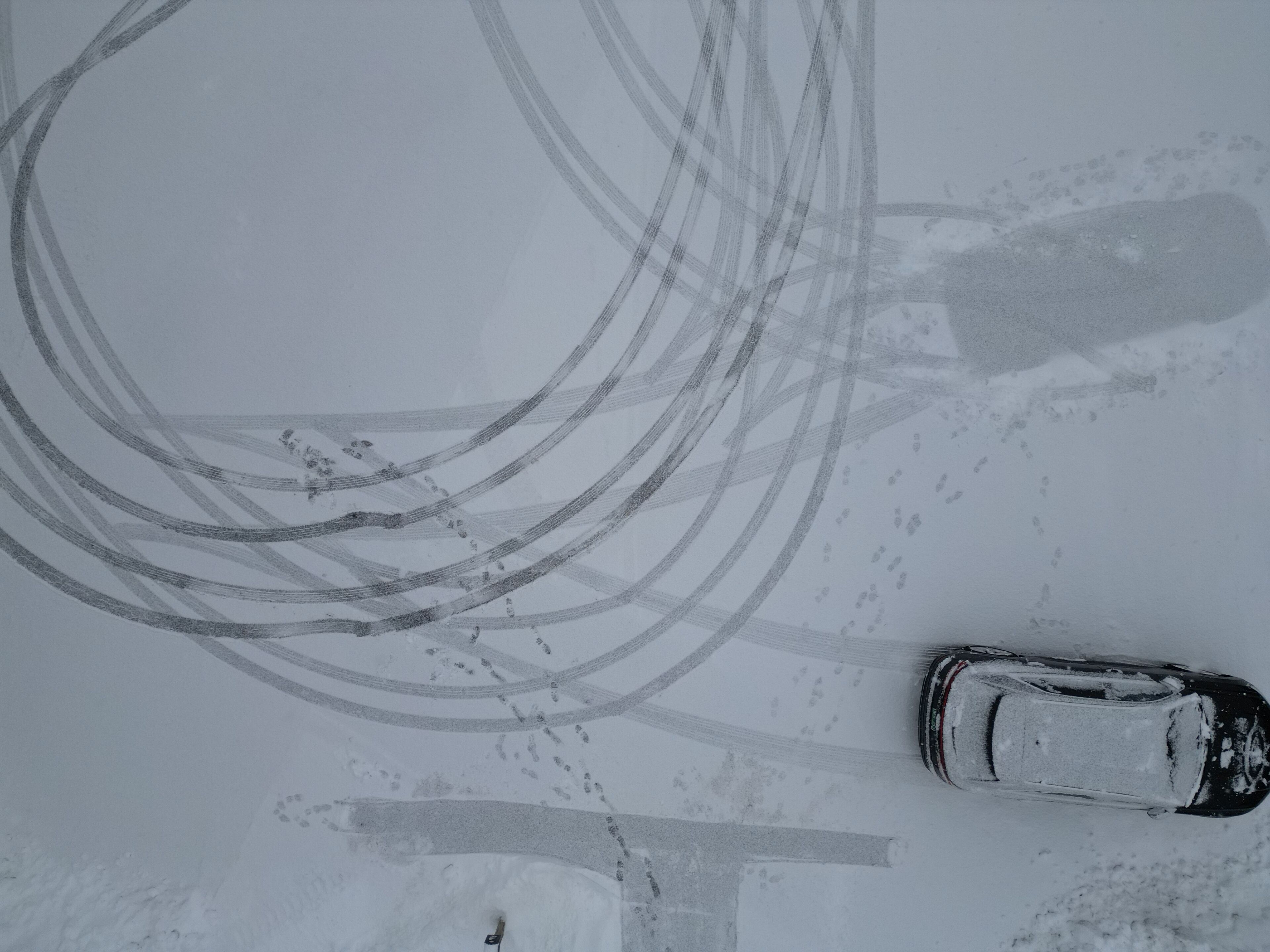 A car parked on a snow-covered road with tire tracks.