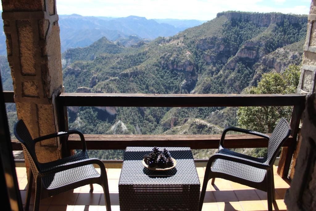 Un balcón con sillas de mimbre y una mesa, con vista a un paisaje montañoso.