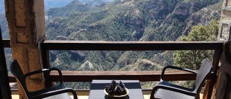 Un balcón con sillas de mimbre y una mesa, con vista a un paisaje montañoso.