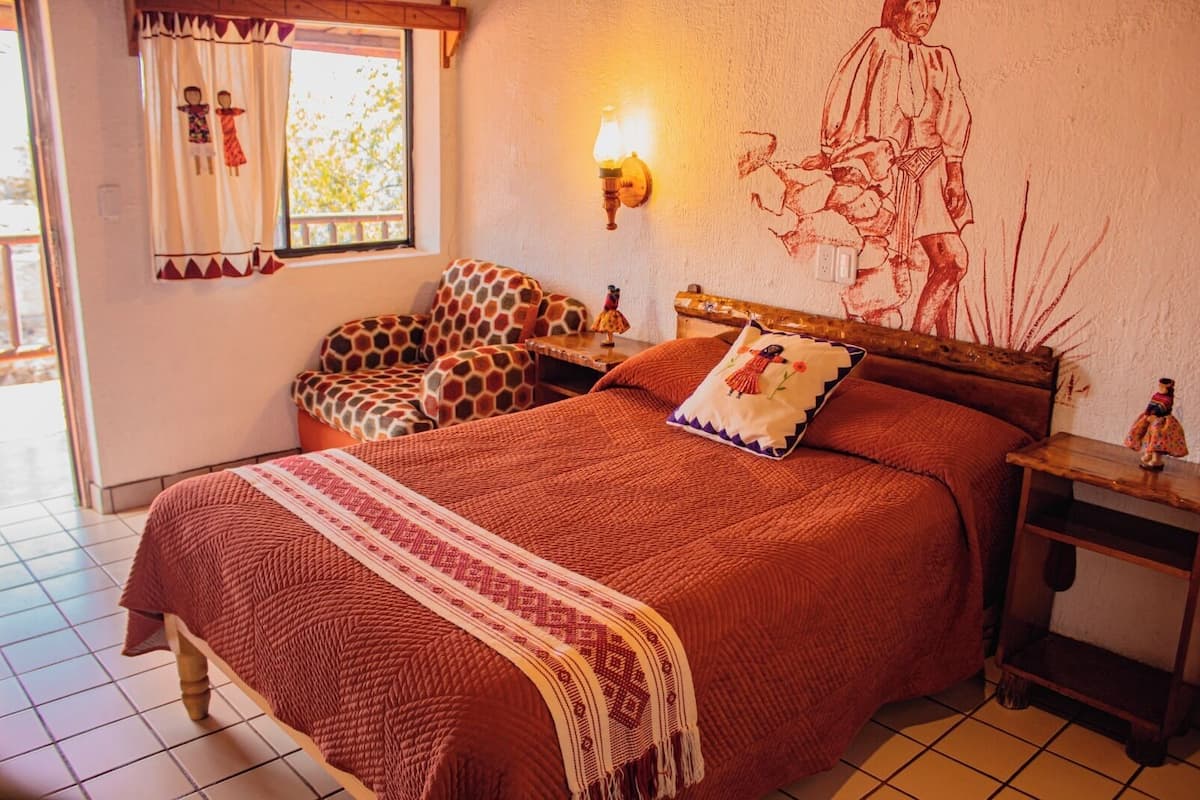 Une chambre confortable avec un grand lit, une table de chevet en bois, une petite table et une lampe fixée au mur.