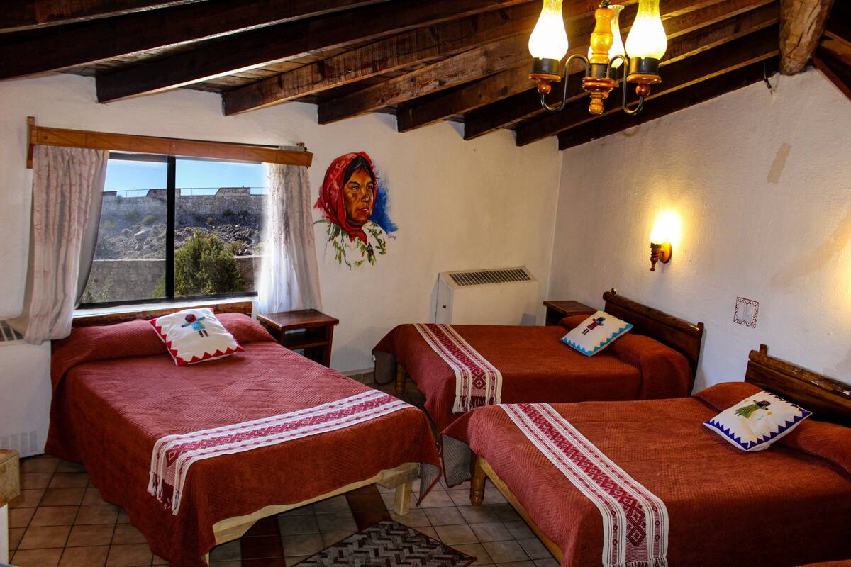 Une chambre avec deux lits, des poutres apparentes, une fenêtre avec des rideaux et un mur orné d’un portrait peint.