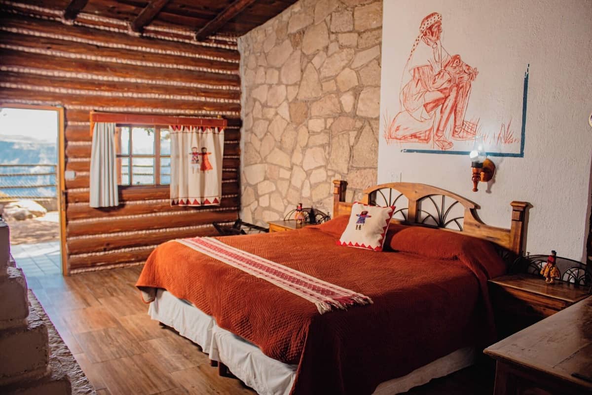 Une chambre confortable dans un chalet en rondins, avec un grand lit, des murs en pierre et une fenêtre avec des rideaux.