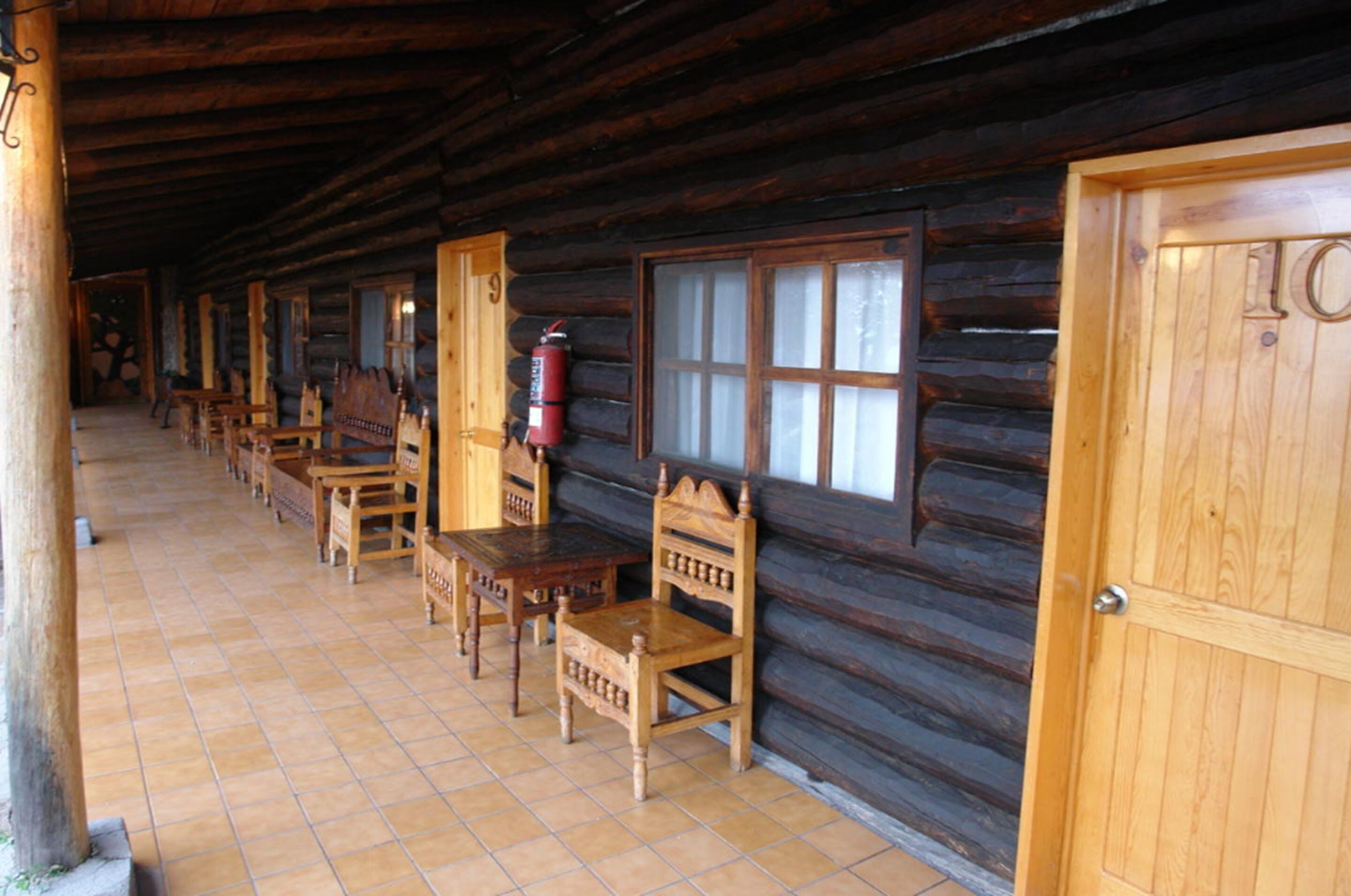 A log cabin with wooden walls, a tiled floor, and a row of wooden benches and tables.