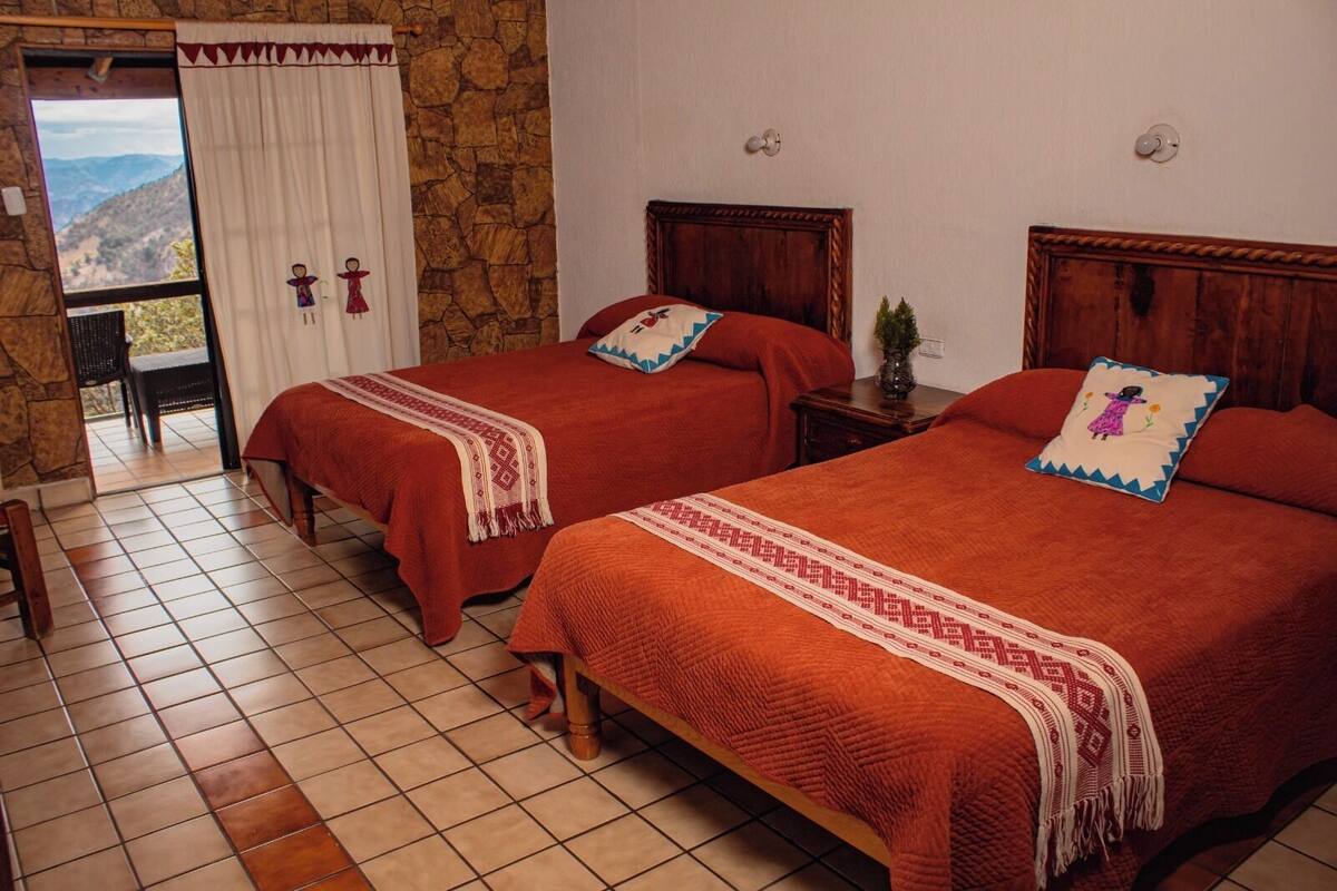 Une chambre avec deux lits, un mur en pierre, une vue par la fenêtre et une porte donnant sur l’extérieur.
