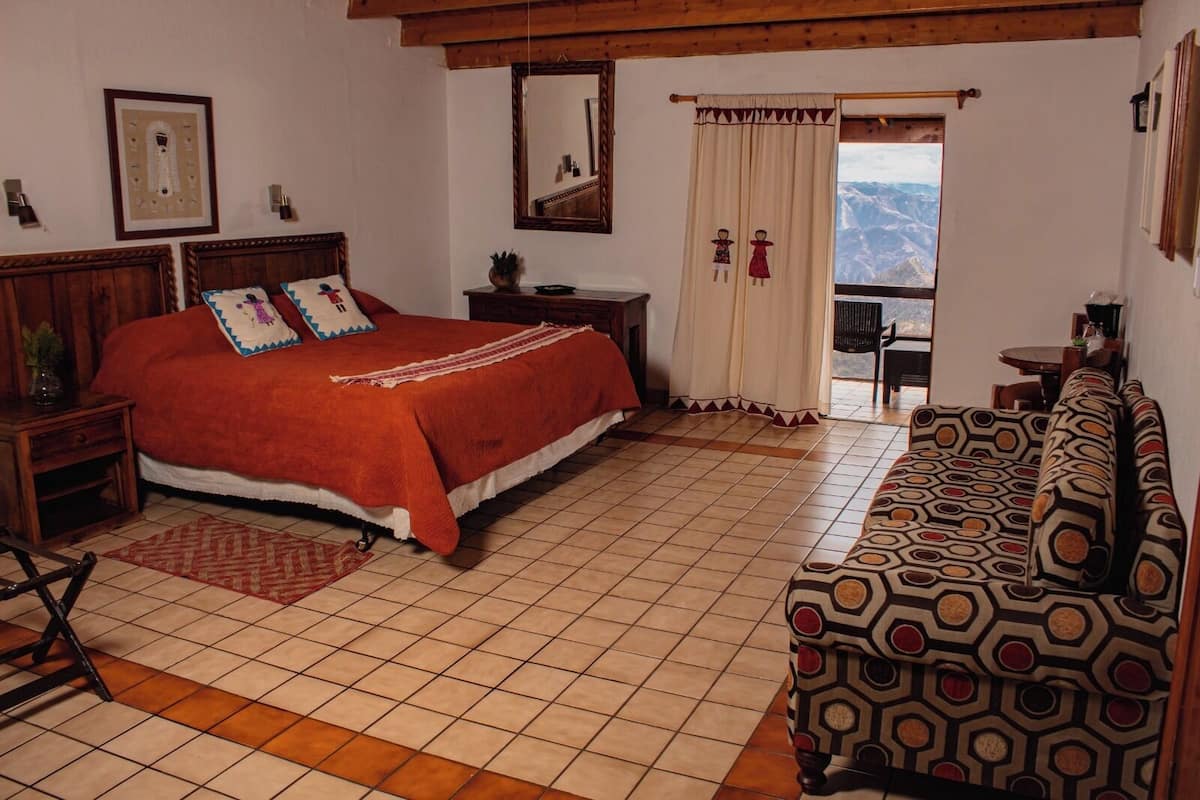 Une chambre avec un grand lit, un canapé, une petite table et une vue sur les montagnes par la fenêtre.