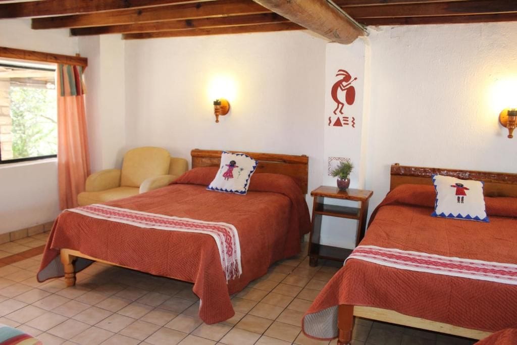 A room with two beds, a chair, and a wall-mounted light fixture.