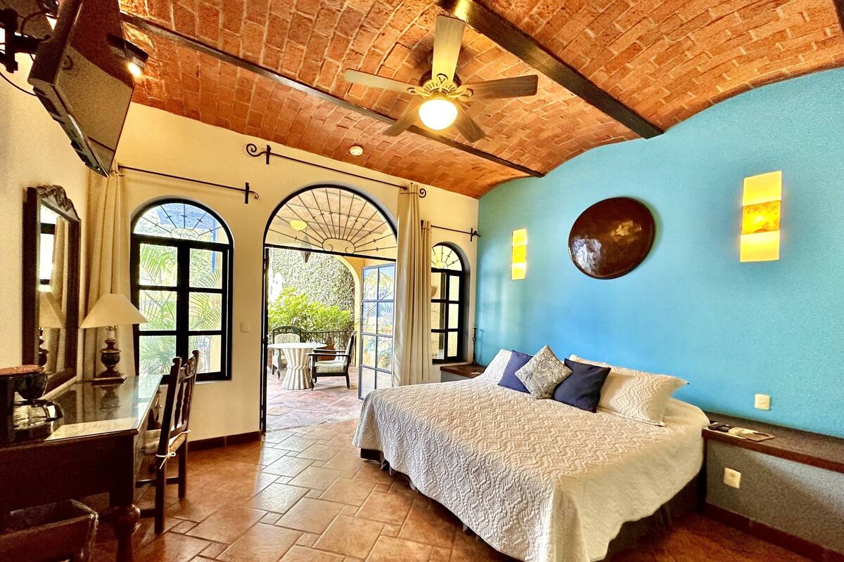 A bedroom with a large bed, a ceiling fan, and a view of a patio with a table and chairs.