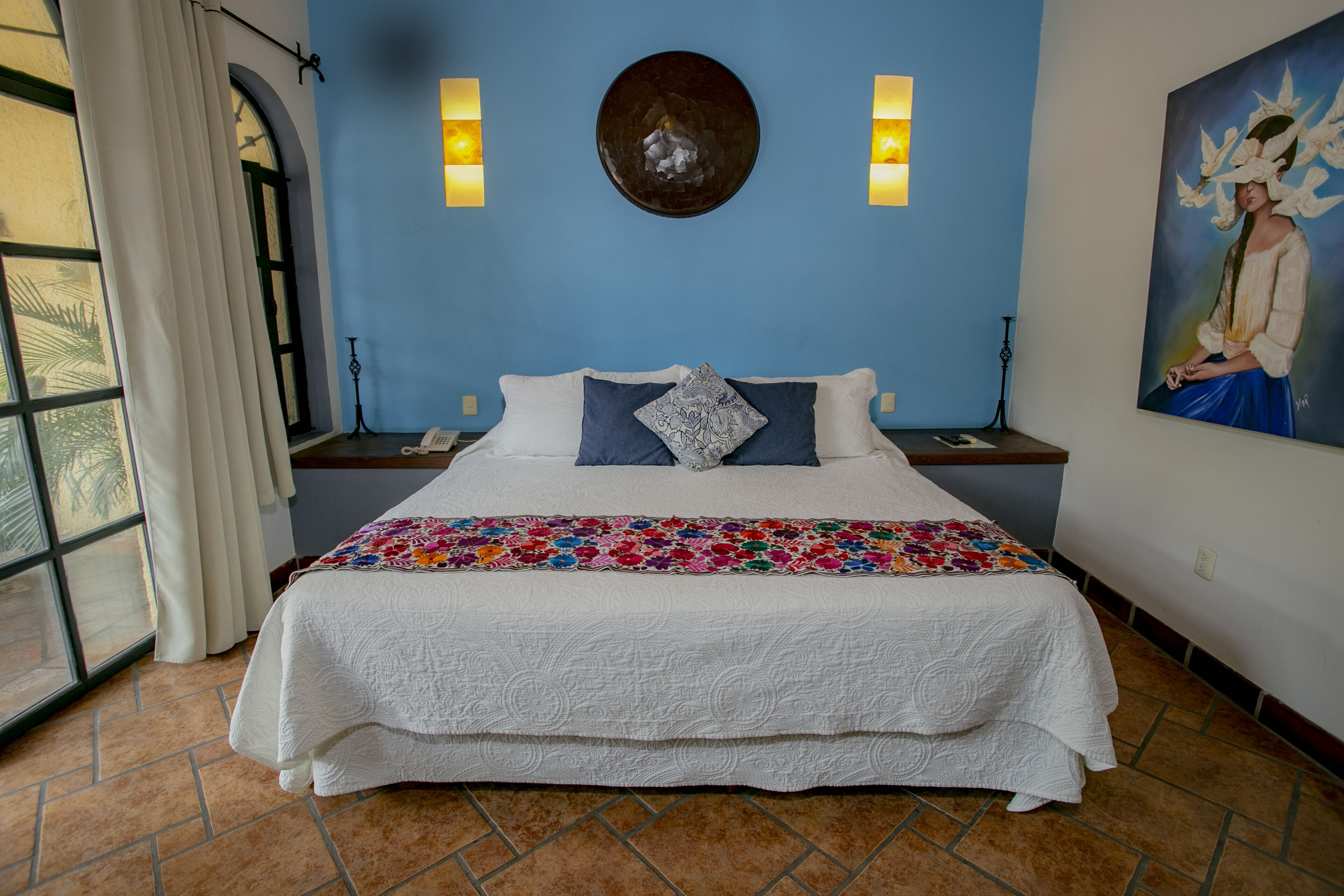 Een slaapkamer met een groot bed, een blauwe muur, een decoratief bord en een schilderij.