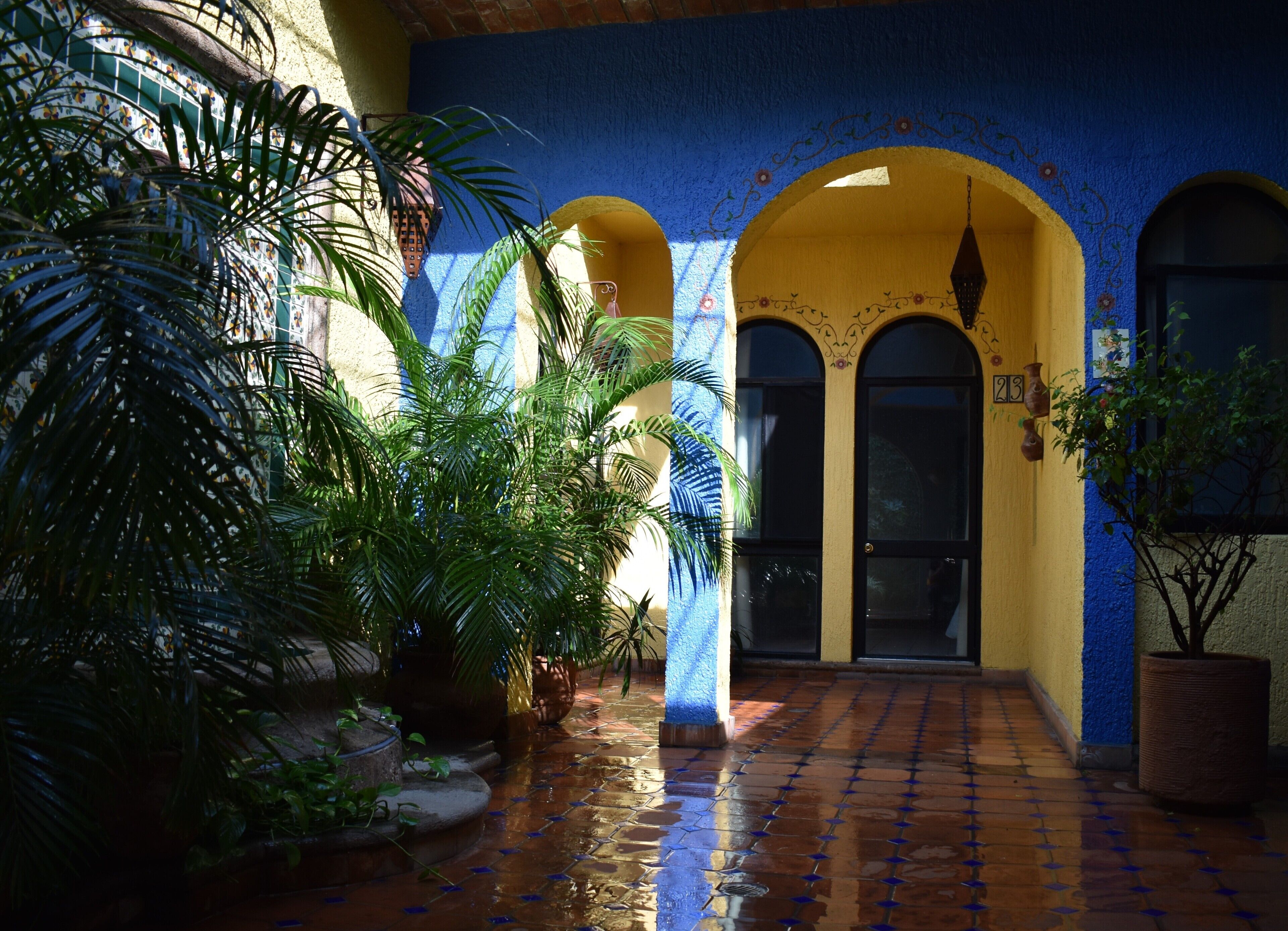 Un patio con suelo de baldosas, una pared azul y una puerta numerada.