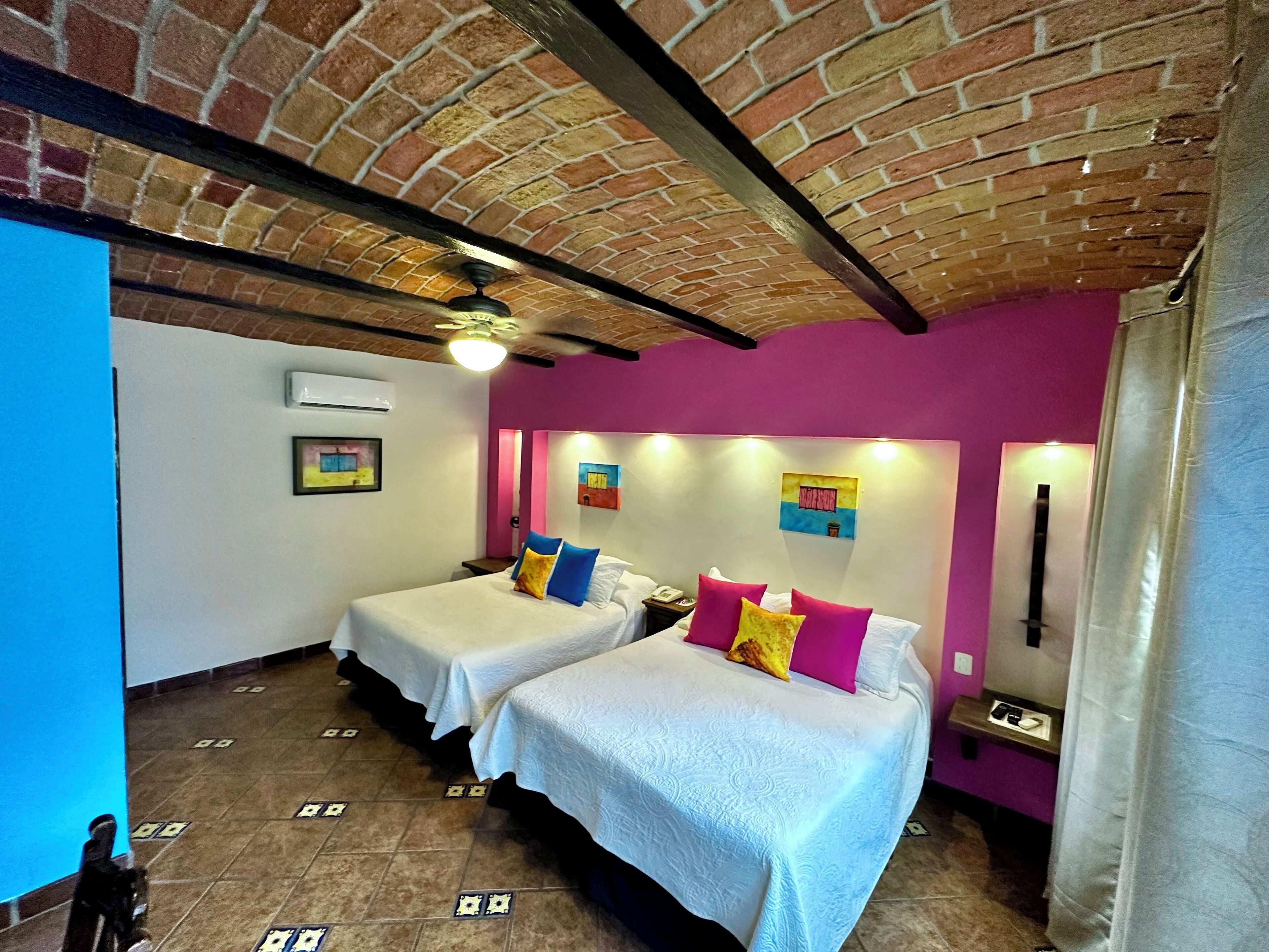 Habitación de hotel con dos camas, techo de ladrillo y pared rosa.