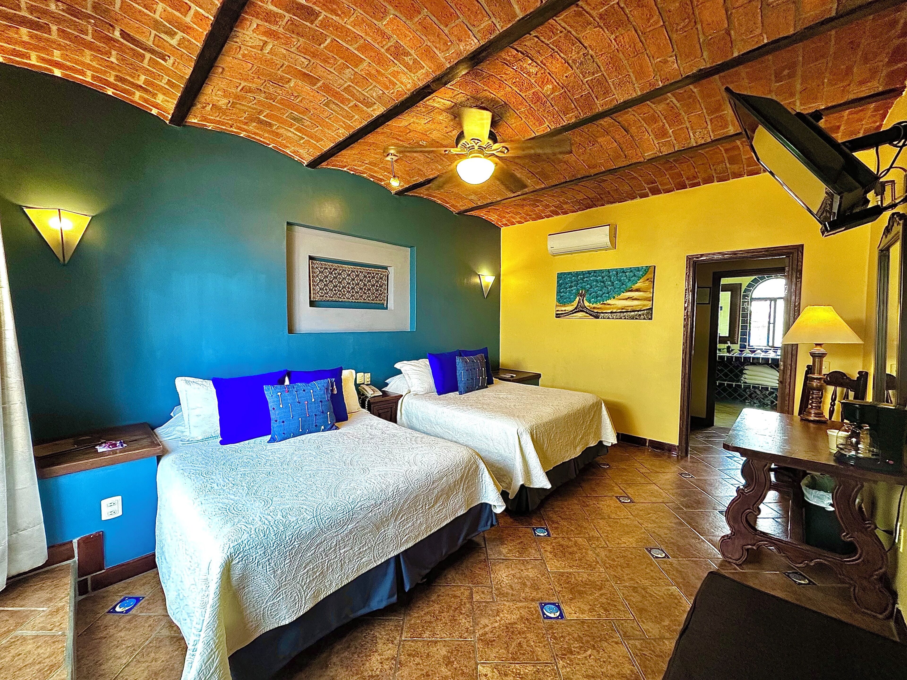 Una habitación con dos camas, techo de ladrillo, un cuadro y suelo de baldosas.