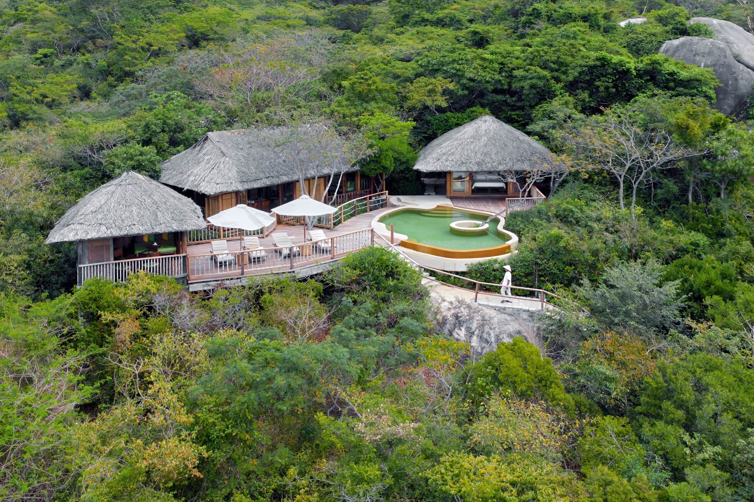 Un resort con villas de techo de paja, una piscina y abundante vegetación.