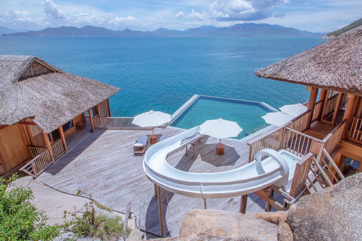 Un resort con piscina infinita, terraza de madera y construcciones con techo de paja.