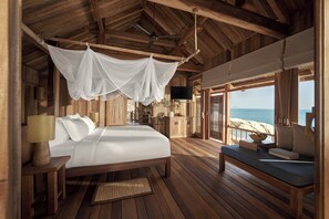 Een houten hutje met een bed, een bank, een televisie en uitzicht op het strand.