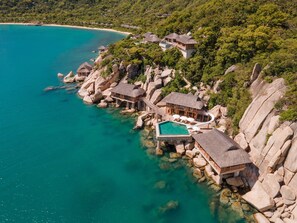 Een resort met bungalows boven het water, verbonden door een brug, een zwembad en een strand.